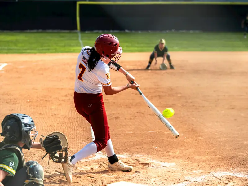 A softball hitter making contact with a pitch.